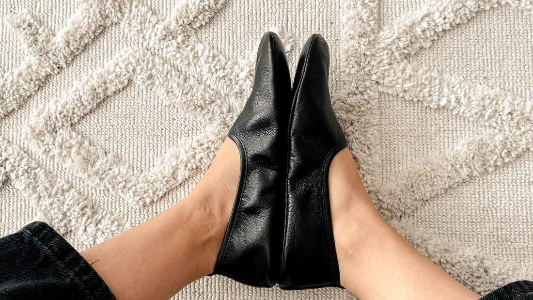 Feet in black leather house shoes on a textured rug at home
